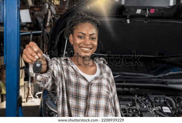 Happy Black African female car owner showing car\
key after fixing vehicle with good service in car repair shop,\
black woman car owner smiling and satisfied with automobile\
maintenance garage\
service