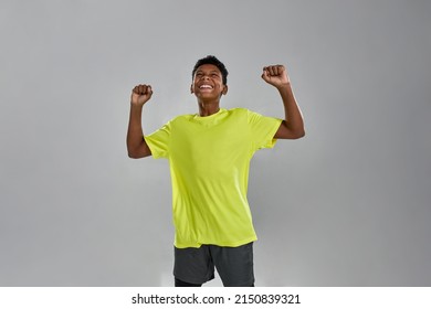 Happy Black Boy With Hands In Air Celebrating His Win Or Triumph. Sportive Male Youngster Wearing Sportswear. Concept Of Modern Child Lifestyle. Isolated On Grey Background. Studio Shoot. Copy Space