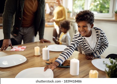 Happy black boy setting dining table while having lunch with his family on holidays.