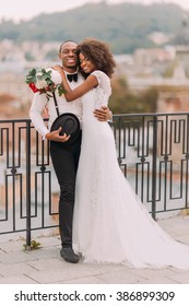 Happy black bride and groom softly hugging on the terrace with cityscape on background