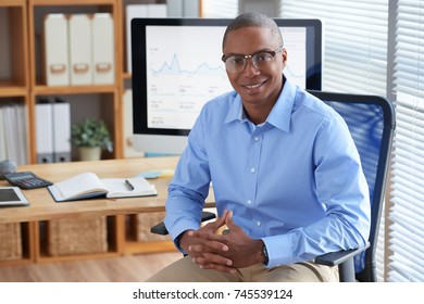 Happy Black businessman sitting in armchair at his office table