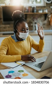 Happy Black Businesswoman Wearing Protective Face Mask And Greeting Someone During Video Call Over Laptop At Home. 