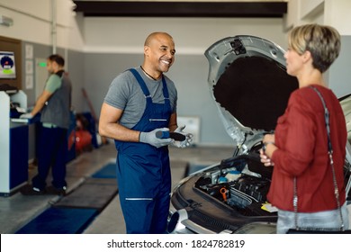 Happy Black Car Mechanic Communicating With His Customer In Auto Repair Shop. 