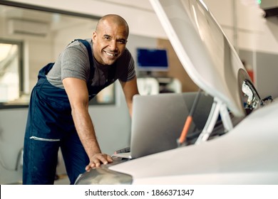 Happy Black Car Mechanic Running Engine Diagnostic On A Laptop In A Workshop And Looking At Camera. 