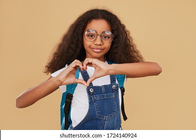 Happy Black Child In Casual Clothes And Glasses Looking At Camera And Showing Heart Gesture On Beige Background