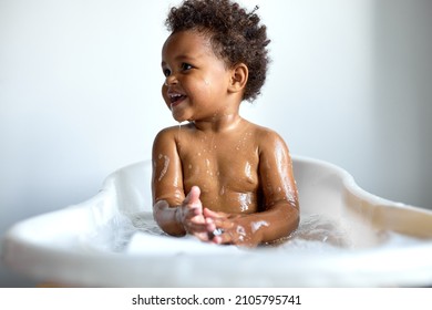 happy black child sitting in bath with foam. Bathing without tears. cute emotional baby is engaged in hygiene procedures, smiling. disinfection, prevention against diseases and viruses