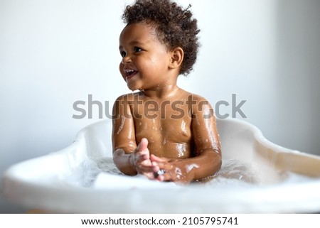 happy black child sitting in bath with foam. Bathing without tears. cute emotional baby is engaged in hygiene procedures, smiling. disinfection, prevention against diseases and viruses
