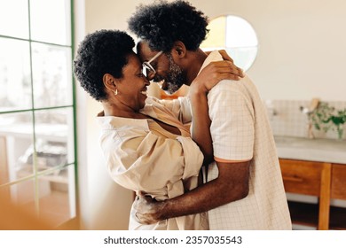 Happy black couple, with afro hair, hold each other in an affectionate hug in their kitchen. Mature husband and wife showing their deep love for each other in an intimate moment. - Powered by Shutterstock