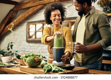 Happy Black Couple Blending Fresh Vegetables And Making Smoothie In The Kitchen.