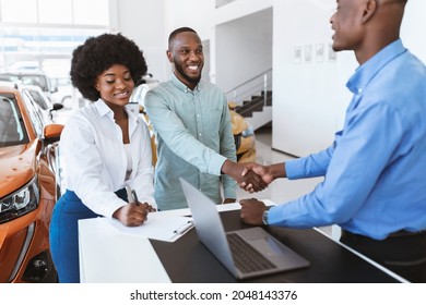 Happy Black Couple Buying New Car, Shaking Hands With Seller, Signing Auto Purchase Agreement At Dealership. Positive African American Clients Getting Automobile At Showroom