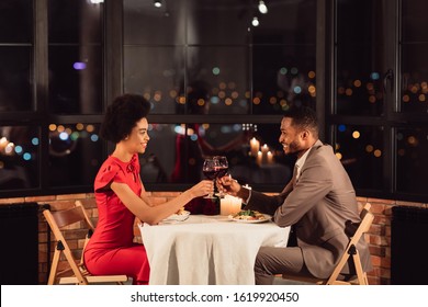 Happy Black Couple Clinking Glasses Drinking Wine And Celebrating Valentine's Day In Restaurant In Evening. Side View