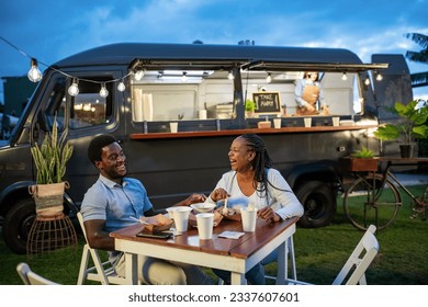 Happy black couple eating near food truck in evening - Powered by Shutterstock