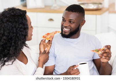 Happy Black Couple Eating Pizza And Drinking Coffee, Relaxing On Weekend At Home