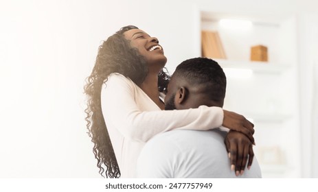 A happy Black couple embraces in their home, the woman laughing and looking up at her partner. - Powered by Shutterstock