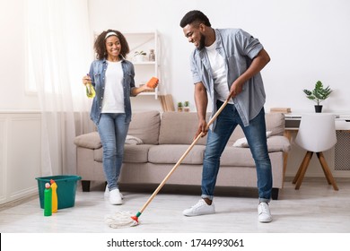 Happy Black Couple Enjoying Cleaning House Together, Man Washing Floor At Home While Woman Using Sponge And Sprayer, Free Space