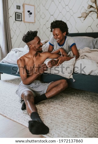 Happy black couple enjoying a conversation in bed while drinking coffee