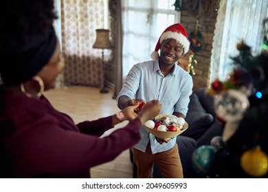 Happy Black Couple Enjoying In Decorating Christmas Tree At Home. Focus Is On Man.