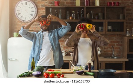 Happy Black Couple Having Fun With Colourful Pepper In Loft Kitchen. Family Preparing Dinner