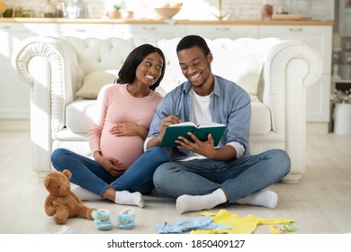 Happy Black Couple Making Checklist Of Baby Things For Maternity Hospital At Home. Loving African American Husband And Wife Getting Ready For Child Delivering, Preparing Stuff For Clinic