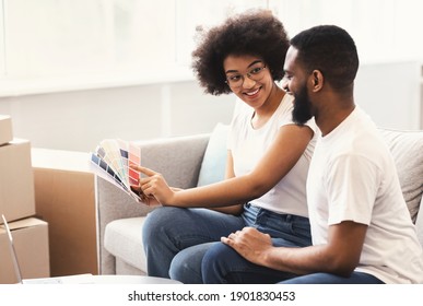 Happy Black Couple Planning Renovation After Moving House, Choosing Color Palettes For Wall Painting Sitting On Couch At Home. Relocation, Real Estate Purchase, Rental And Ownership Concept