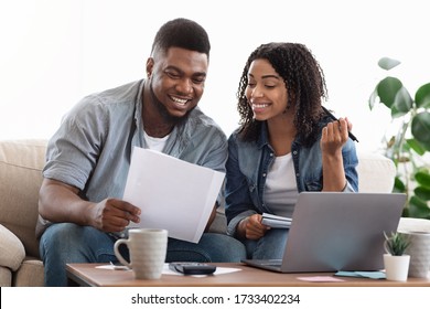 Happy Black Couple Reading Financial Documentation At Home While Planning Family Budget Together, Accounting Their Savings