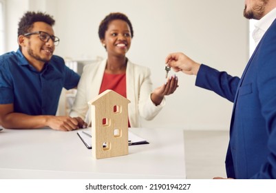 Happy Black Couple Relocating To New Apartment. Realtor Or Real Estate Agent Gives Key To Two Smiling First Time House Owners. Husband And Wife Sign Rental Or Lease Agreement And Take Keys To New