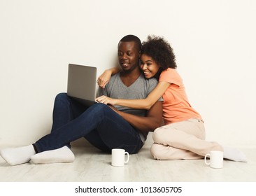 Happy Black Couple Shopping Online, Making Order With Laptop While Sitting At Home Floor In Empty Living Room, Copy Space, Isolated