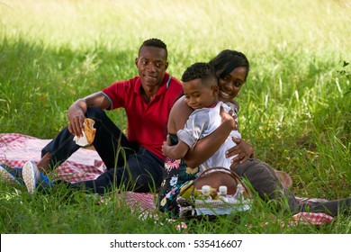 Happy Black Couple With Son In City Park. African American Family With Young Man, Woman And Child Doing Picnic, Having Fun Outdoor.