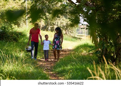 Happy Black Couple With Son Walking In City Park. African American Family With Young Man, Woman And Child Doing Picnic, Having Fun Outdoor.