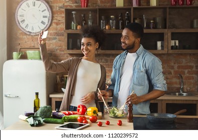 Happy black couple taking photo with smartphone while preparing healthy salad at kitchen