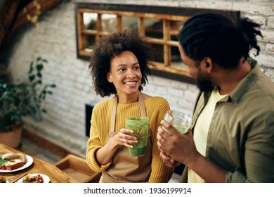 Happy black couple talking while drinking green smoothie in the kitchen. Focus is on woman. 