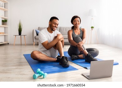 Happy Black Couple Watching Sports Video On Laptop After Yoga Practice, Communicating With Personal Trainer Online At Home, Full Length. Fit Young Family Leading Healthy Active Lifestyle