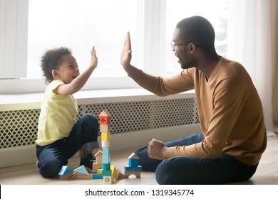 Happy Black Dad And Cute Toddler Son Giving High Five Playing With Wooden Blocks On Floor At Home, Little Kid Boy Enjoying Game With African Father, Daddy Child Clapping Hands Having Fun Together