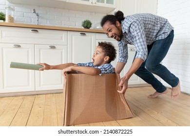 Happy Black Dad Driving Cardboard Box With Excited Little Son Inside, Playing With Kid At Home, Enjoying Active Games, Leisure, Entertainment After Moving Into New Apartment. Family, Relocation