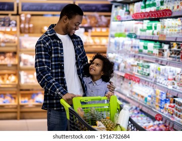 Happy black dad and his pretty little daughter with shopping trolley having great time buying groceries at big mall. African American parent with kid purchasing foodstaff at hypermarket - Powered by Shutterstock