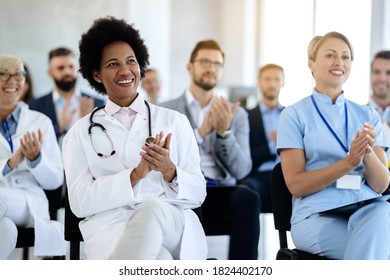 Happy Black Doctor And Her Colleagues Clapping Their Hands After Successful Presentation In Board Room. 