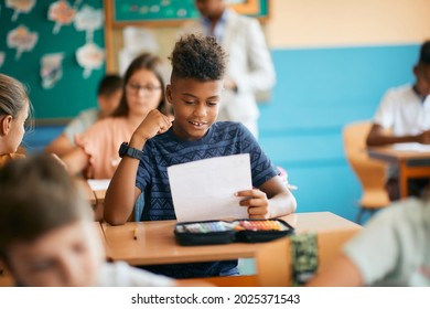 Happy black elementary student celebrating getting a good grade in the classroom at school.  - Shutterstock ID 2025371543