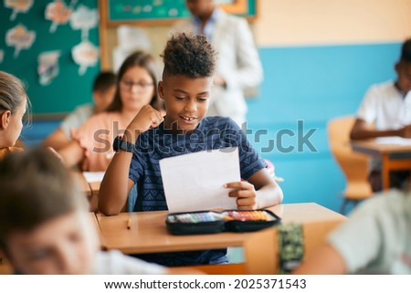 Happy black elementary student celebrating getting a good grade in the classroom at school. 
