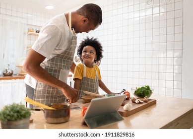 Happy Black Family. African American Father And Little Son Doing Online Cooking With Digital Tablet In Kitchen At Home