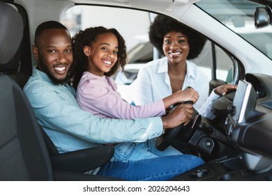 Happy Black Family Buying New Car, Test Driving Automobile, Smiling At Camera In Auto Dealership. Afro Parents And Their Daughter Selecting Luxury Vehicle At Showroom Store