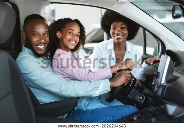 Happy black\
family buying new car, test driving automobile, smiling at camera\
in auto dealership. Afro parents and their daughter selecting\
luxury vehicle at showroom\
store