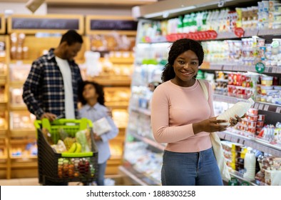 Happy Black Family With Child Shopping For Products At Dairy Section Of Supermarket, Copy Space. Positive African American Parents With Kid Purchasing Groceries At Huge Mall