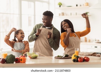 Happy Black Family Cooking And Having Fun Standing In Modern Kitchen At Home. Parents And Daughter Spending Time Together Preparing Dinner Making Vegetable Salad Indoors. Healthy Nutrition Concept