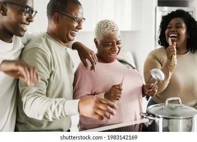 Happy black family dancing while cooking vegan food inside kitchen at home - Focus on mother face