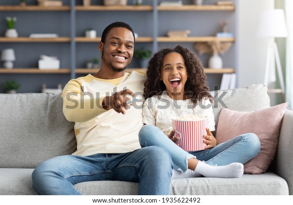 Happy black family father and daughter watching\
movie together