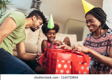 Happy Black Family At Home. African American Father, Mother And Child Celebrating Birthday, Having Fun At Party. Young Woman Giving Gift To Daughter