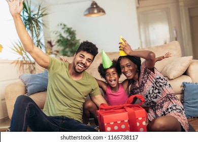 Happy Black Family At Home. African American Father, Mother And Child Celebrating Birthday, Having Fun At Party. Young Woman Giving Gift To Daughter