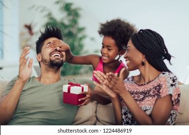 Happy Black Family At Home. African American Father, Mother And Child Celebrating Birthday, Having Fun At Party.Daughter Giving Gift To Father.