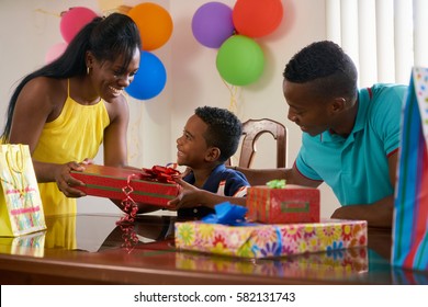 Happy Black Family At Home. African American Father, Mother And Child Celebrating Birthday, Having Fun At Party. Young Woman Giving Gift To Son.