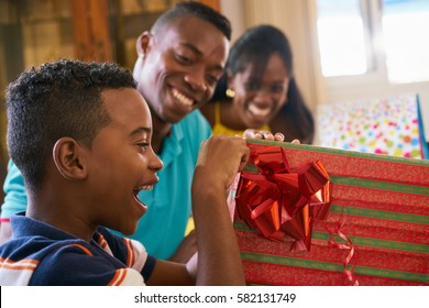 Happy Black Family At Home. African American Father, Mother And Child Celebrating Birthday, Having Fun At Party. Young Boy Opening Gifts And Smiling.